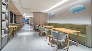 Un interior moderno con una larga fila de mesas y sillas, un área de estar central y una pared con un elemento decorativo circular.