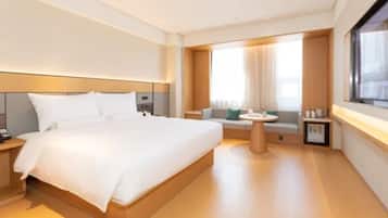 A modern hotel room with a large bed, a small seating area, and a window with curtains.