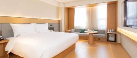 A modern hotel room with a large bed, a small seating area, and a window with curtains.