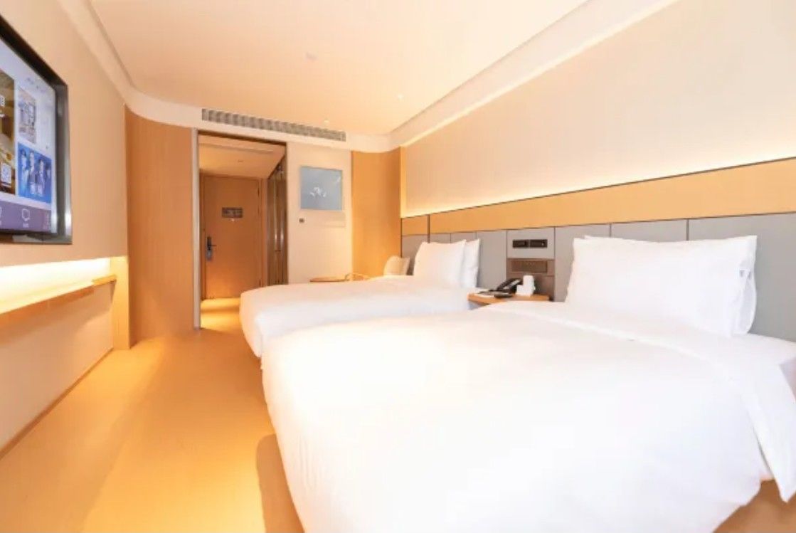 Camera d'albergo con due letti, un comodino con il telefono, una TV a parete e una porta che dà su un'altra stanza.