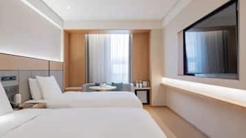 A modern hotel room with two beds, a small round table, a TV, and a large window with curtains.