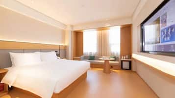 A modern hotel room with a large bed, a small seating area, a TV, and a window with curtains.