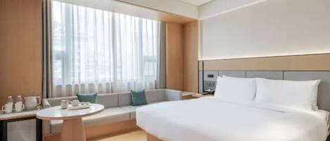 A modern hotel room with a large bed, a seating area with a table, and a large window.