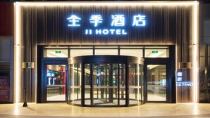 Ein Hotel mit Eingangsbereich, einer Drehtür, beleuchteten Schildern und einem sichtbaren KFC-Restaurant im Hintergrund.