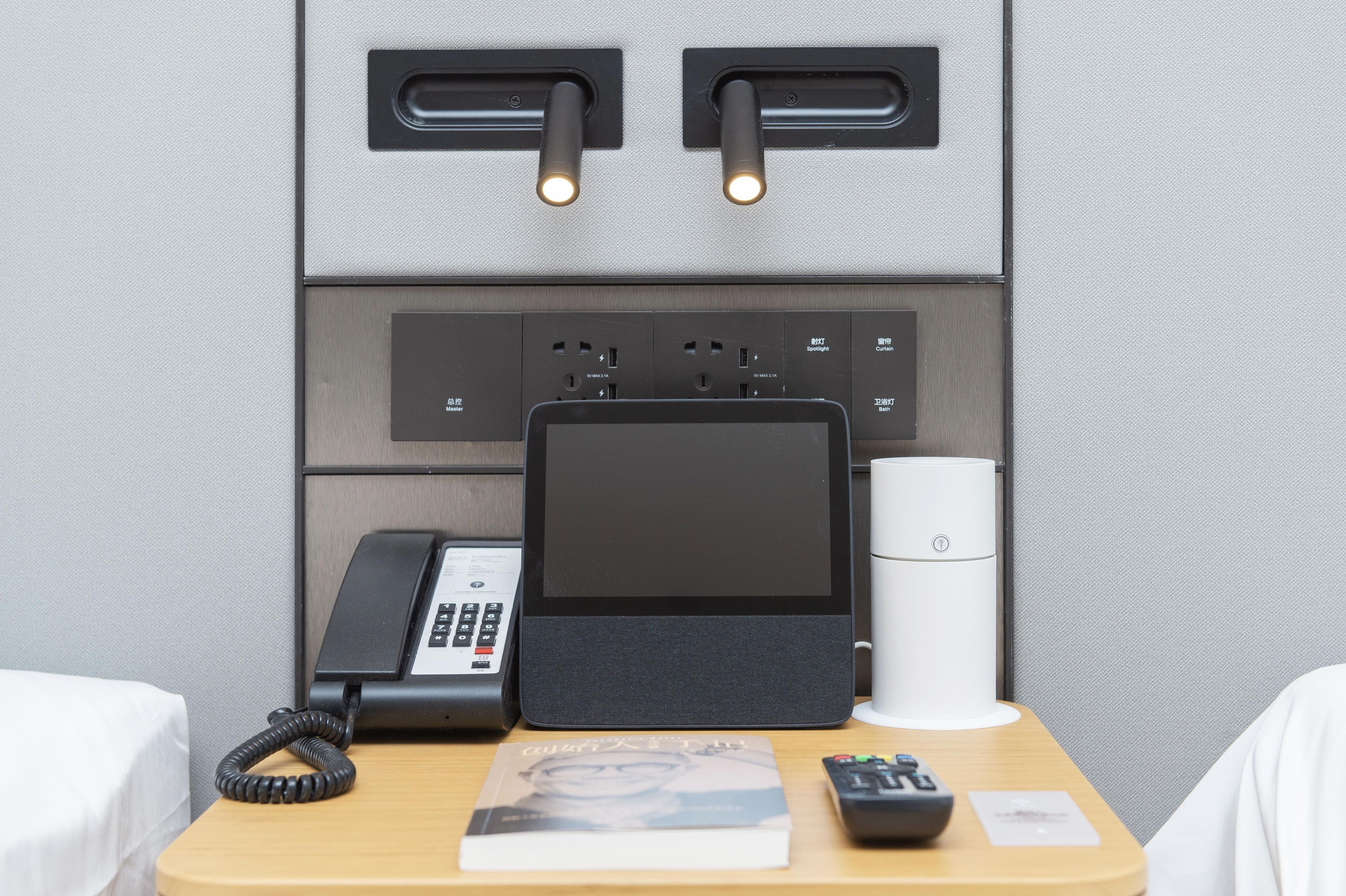 Habitación de hotel con escritorio, teléfono, tableta, control remoto, libro y cafetera.