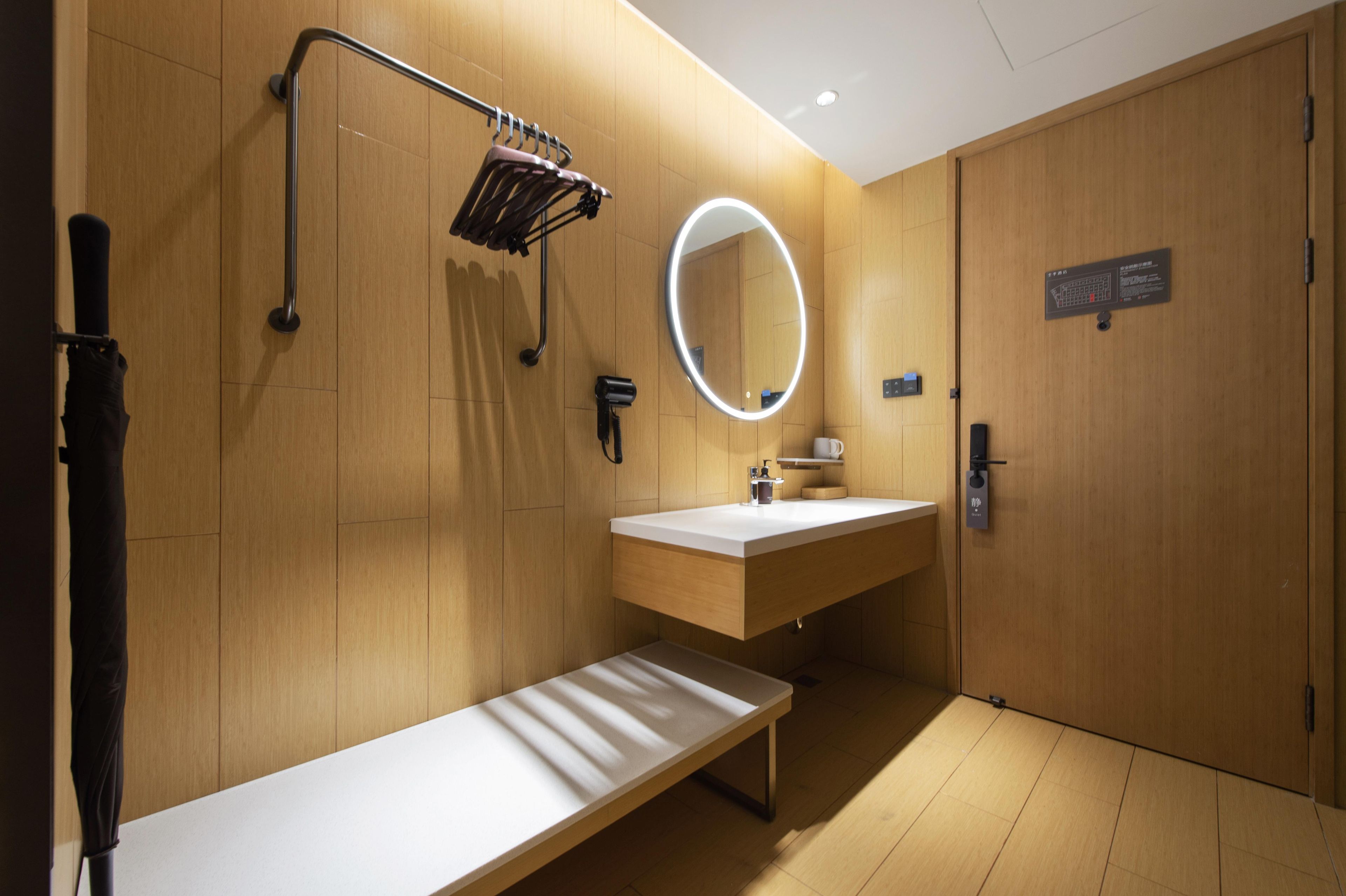 A modern bathroom with a wooden vanity, a bench, a hand dryer, a mirror, and a door with a sign.