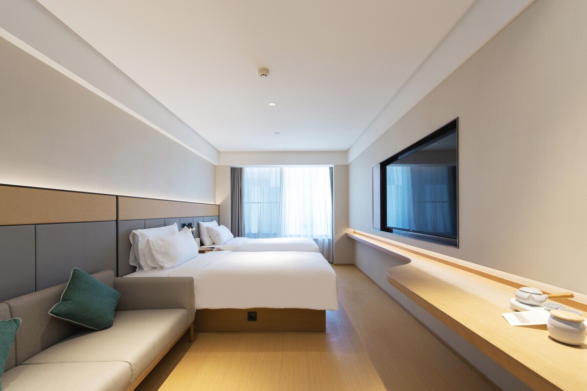 A hotel room with a bed, a sofa, a TV, and a window.