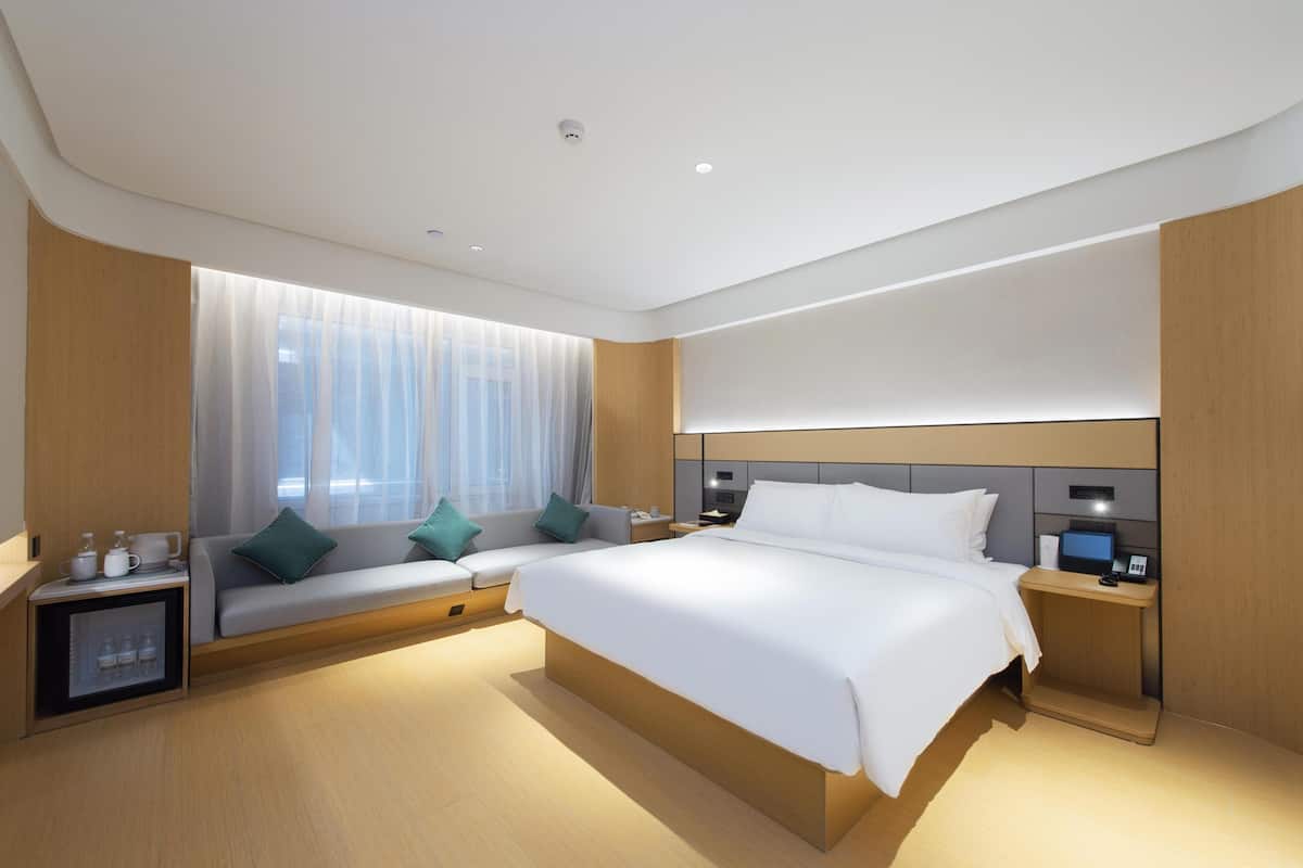 Una habitación de hotel moderna con una cama grande, un sofá, una mesita de noche y un pequeño armario.