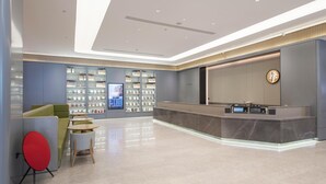 Eine moderne Hotelhalle mit Empfangstresen, Sitzgelegenheiten und einem digitalen Bildschirm.