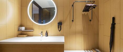 A modern bathroom with a round mirror, a white sink, a towel rack, and a bench.