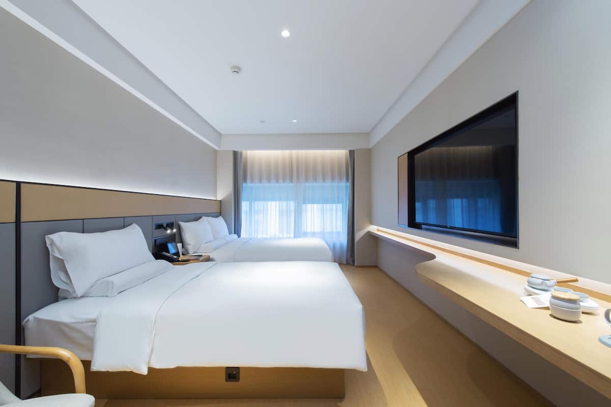 Una habitación de hotel con cama, mesita de noche, televisor y ventana con cortinas.