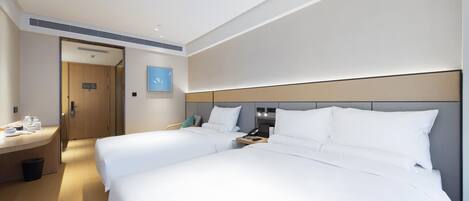 Une chambre d’hôtel avec deux lits, un bureau, une chaise, une poubelle et une porte donnant sur une autre chambre.
