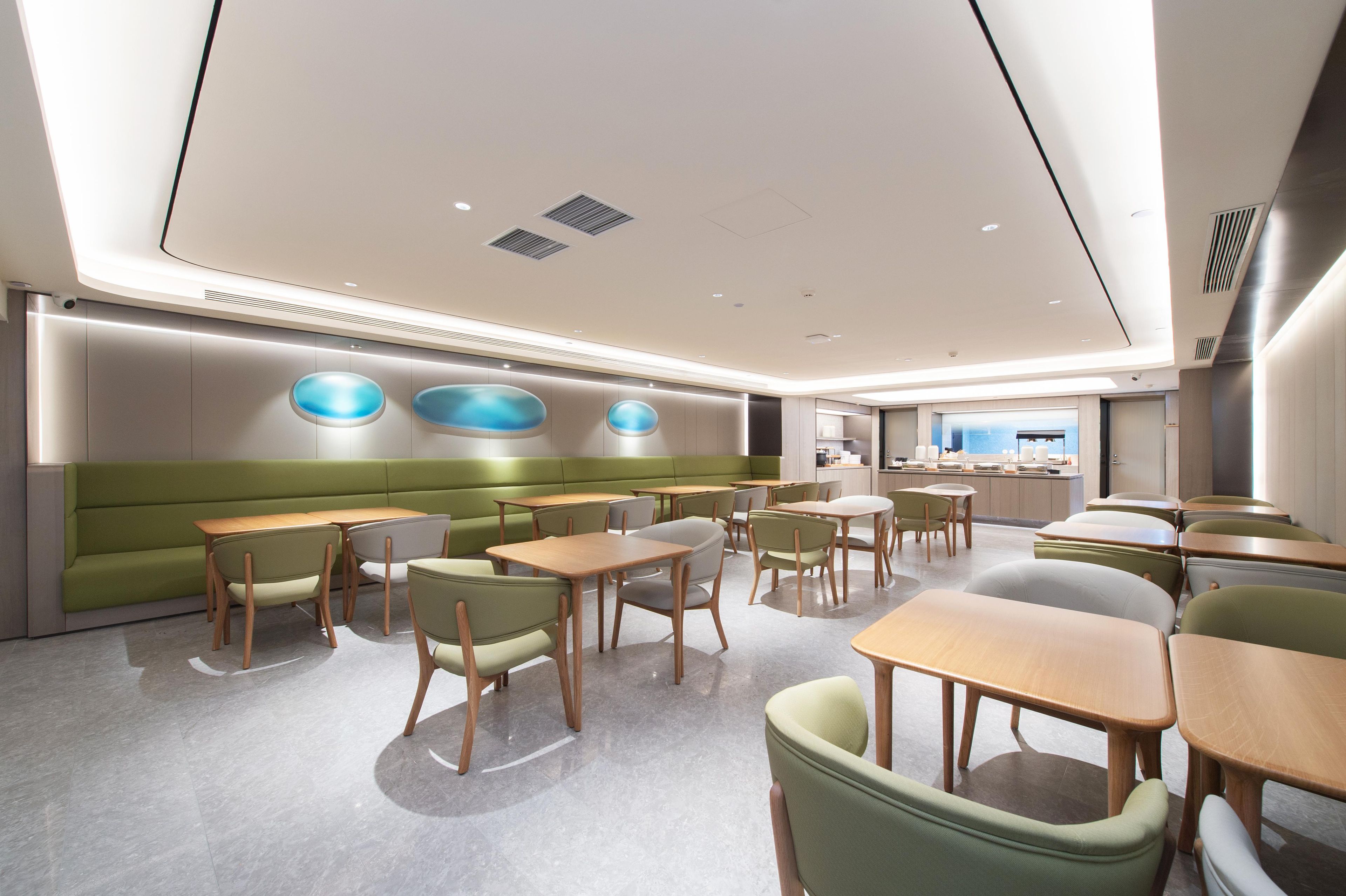 A modern dining area with booths and tables, a green accent wall, and a kitchen in the background.