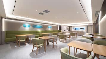 A modern dining area with booths and tables, a green accent wall, and a kitchen in the background.