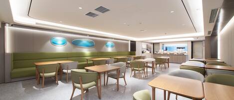 A modern dining area with booths and tables, a green accent wall, and a kitchen in the background.