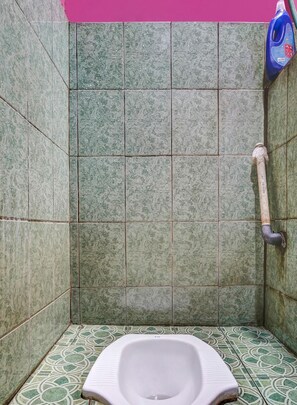 A small, tiled bathroom with a toilet, a handwashing station, and a blue bottle of hand soap. - OYO 91128 Desa Wisata Lebakmuncang Ciwidey Syariah (Ciwidey)