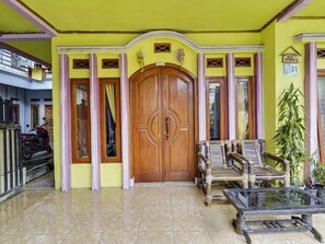 A yellow building with a large wooden door, a glass table, and a bamboo bench. - OYO 91128 Desa Wisata Lebakmuncang Ciwidey Syariah (Ciwidey)