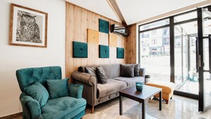 Ein modernes Wohnzimmer mit Sofa, Sessel und Couchtisch, Holzwandverkleidung und einem großen Fenster.