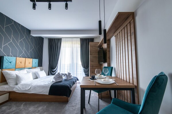 A modern hotel room with a bed, a dining table, and a TV.