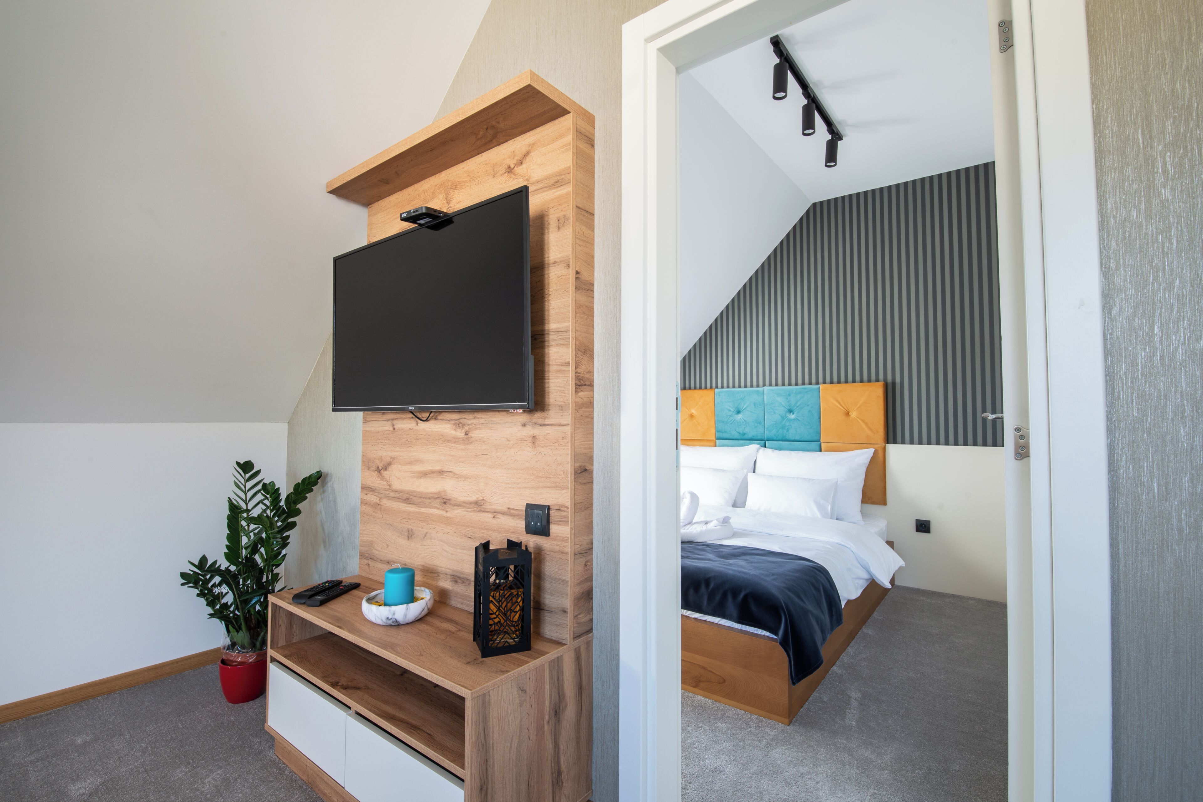 A bedroom with a bed, a TV mounted on a wooden wall, a bedside table, and a potted plant.
