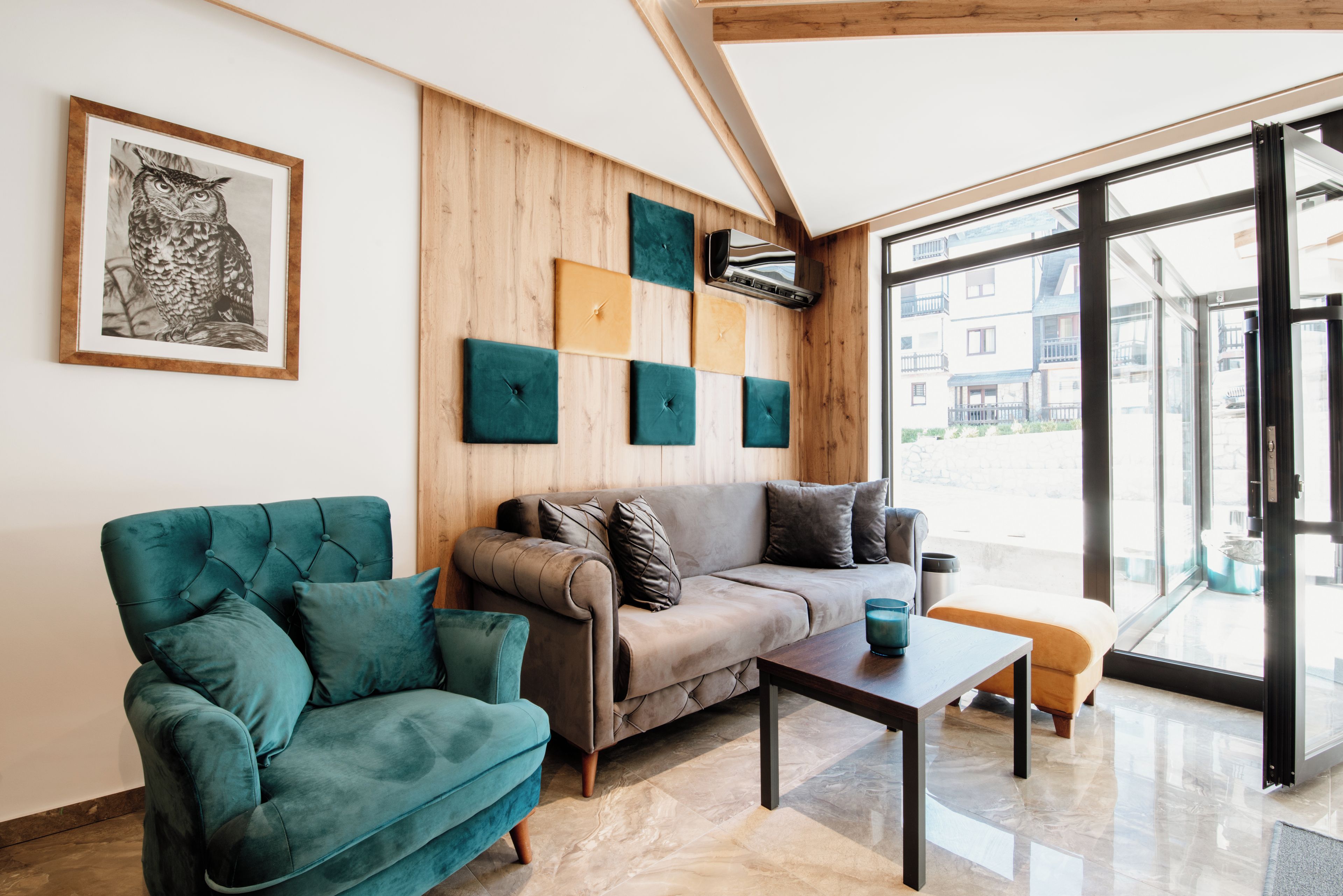 A modern living room with a sofa, armchair, and coffee table, wooden panel walls, and a large window.