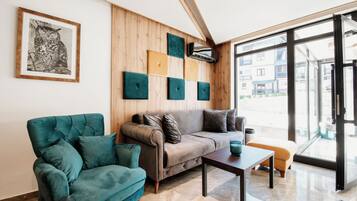 A modern living room with a sofa, armchair, and coffee table, wooden panel walls, and a large window.