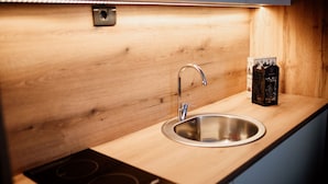 A modern kitchen with a stainless steel sink, wooden countertop, and a built-in induction cooktop. - Hotel Djina (Raška)