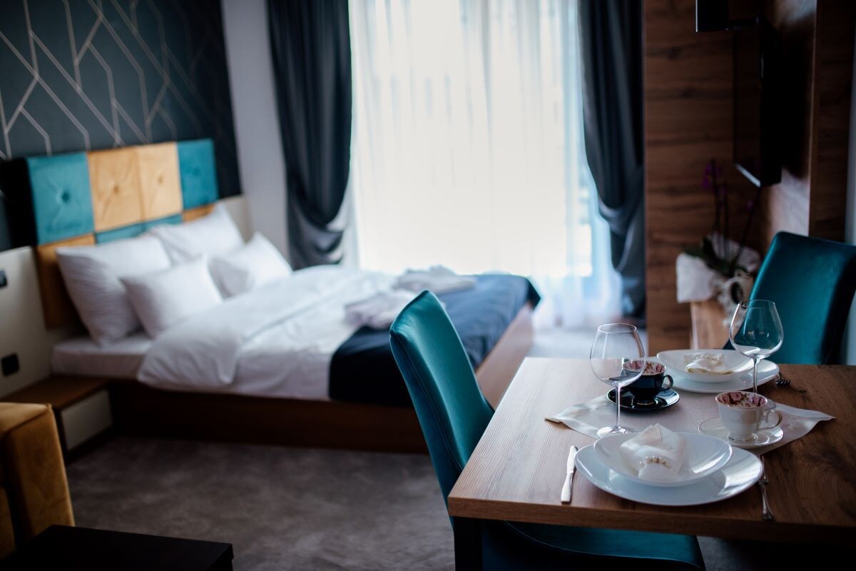 A hotel room with a bed, a dining table set with plates, glasses, and a cup, and a TV mounted on the wall.