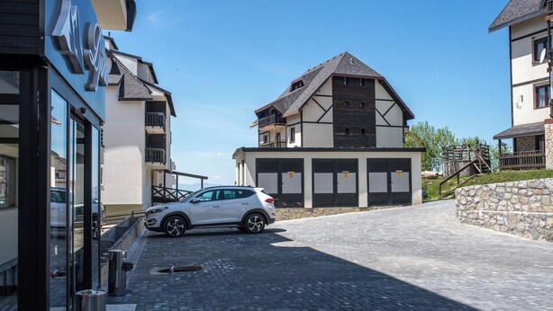 A modern building with a car parked in front, a stone wall, and a clear sky. - Hotel Djina (Raška)