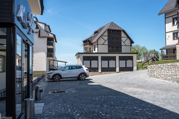 A modern building with a car parked in front, a stone wall, and a clear sky.