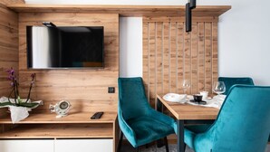 Ein modernes Zimmer mit einem an der Holzwand befestigten Flachbildfernseher, einem Esstisch mit türkisfarbenen Stühlen und einer kleinen Ablage mit einer Uhr und einer Orchideenpflanze.