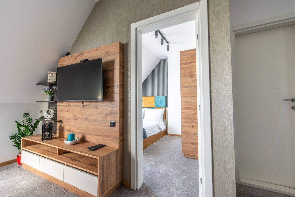 Un dormitorio moderno con televisor integrado, una consola de madera, cama con cabecero colorido y una puerta que da a otra habitación.