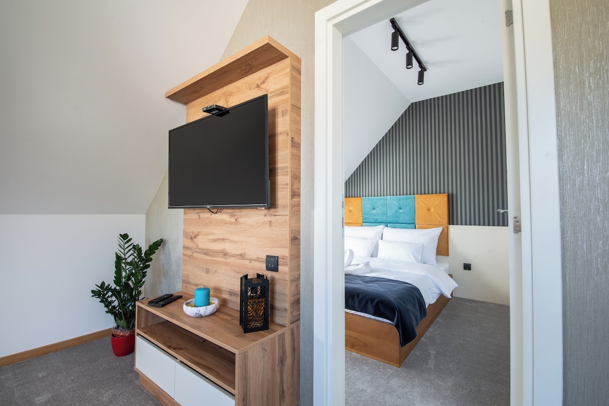 A bedroom with a bed, a TV mounted on a wooden wall, a bedside table, and a potted plant.