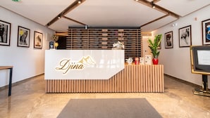 A reception desk with a logo, wooden slats, and framed pictures on the walls. - Hotel Djina (Raška)