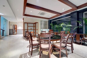 A spacious dining area with a round table and wooden chairs, a large window with a view of palm trees, and a modern interior design. - Amritara Sadka, Amritsar Golden Temple (Amritsar)
