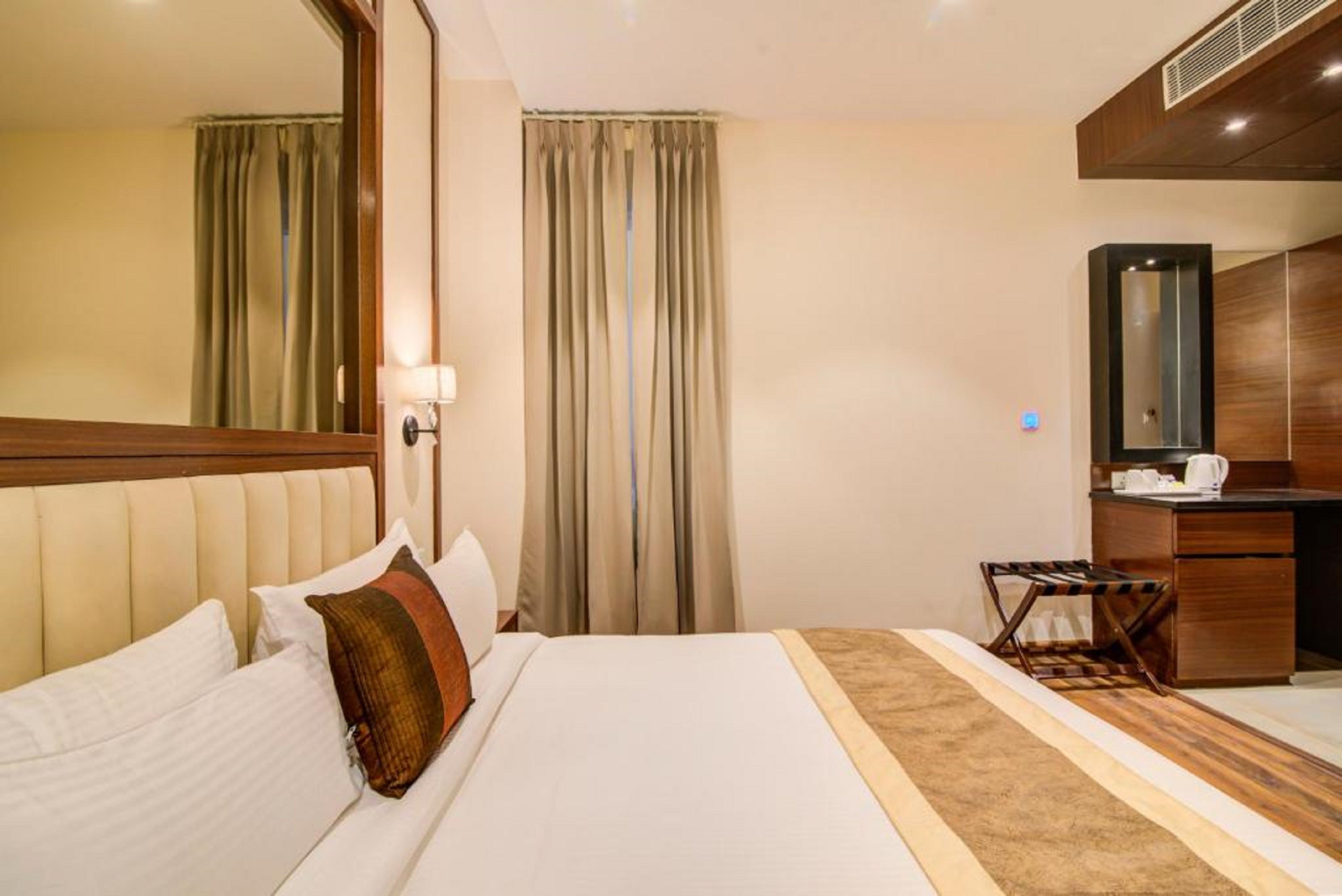 A hotel room with a large bed, a desk, a mirror, and a window with curtains.
