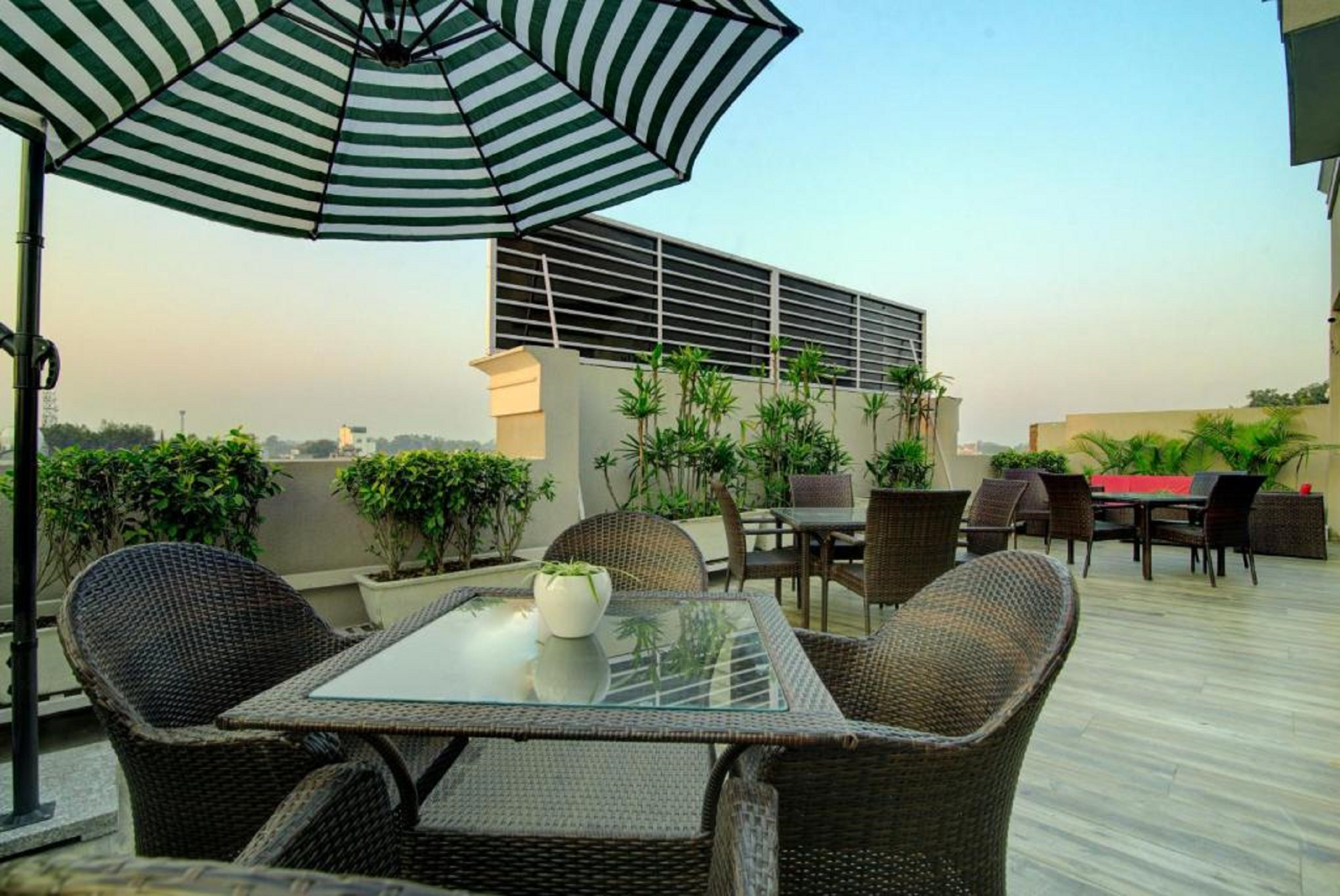 A rooftop patio with wicker furniture, a glass table, and a striped umbrella.