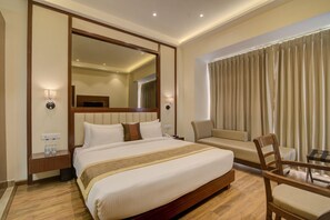 A hotel room with a large bed, a sofa, a wooden chair, a desk, and a mirror. - Amritara Sadka, Amritsar Golden Temple (Amritsar)