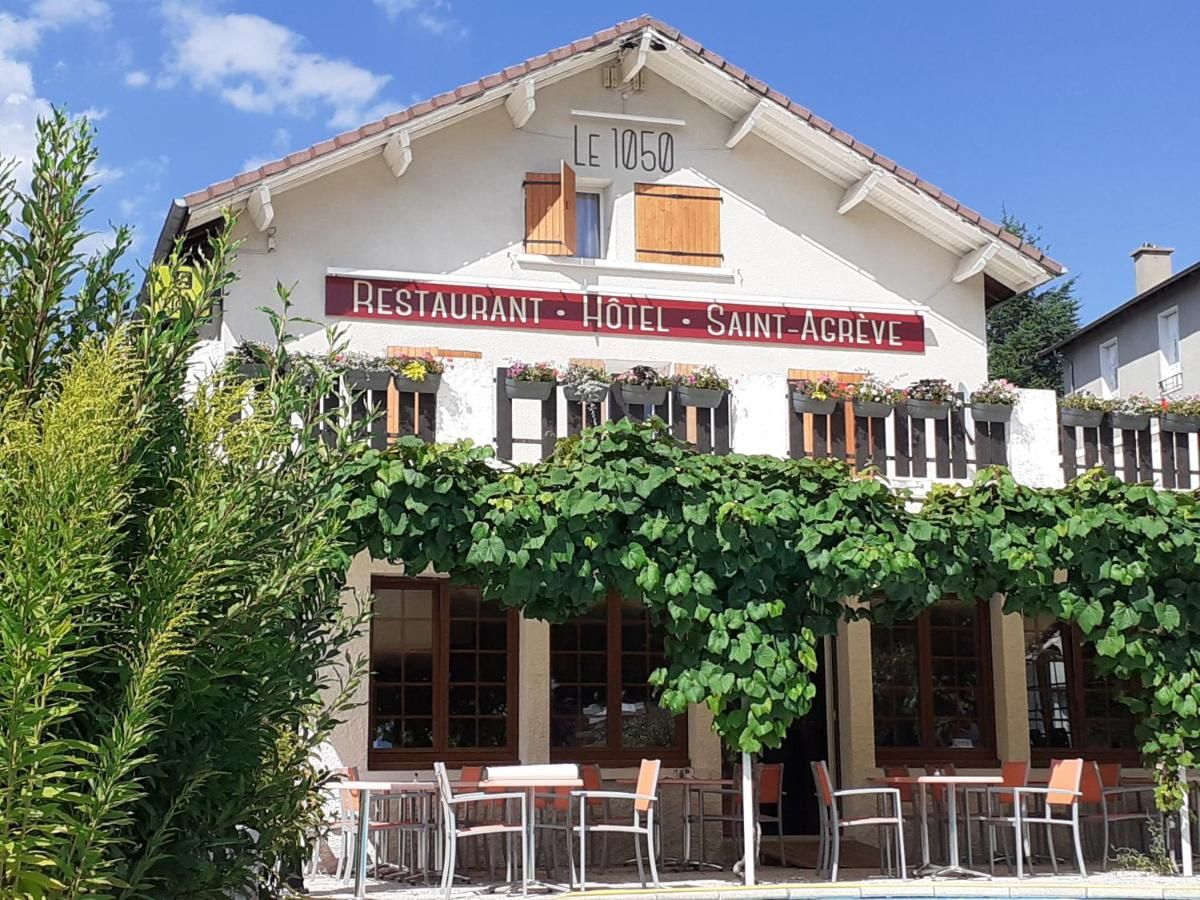 A building labeled 'LE 1050 RESTAURANT HOTEL SAINT-AGREVE' with outdoor seating and a vine-covered facade.