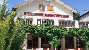 A building labeled 'LE 1050 RESTAURANT HOTEL SAINT-AGREVE' with outdoor seating and a vine-covered facade.