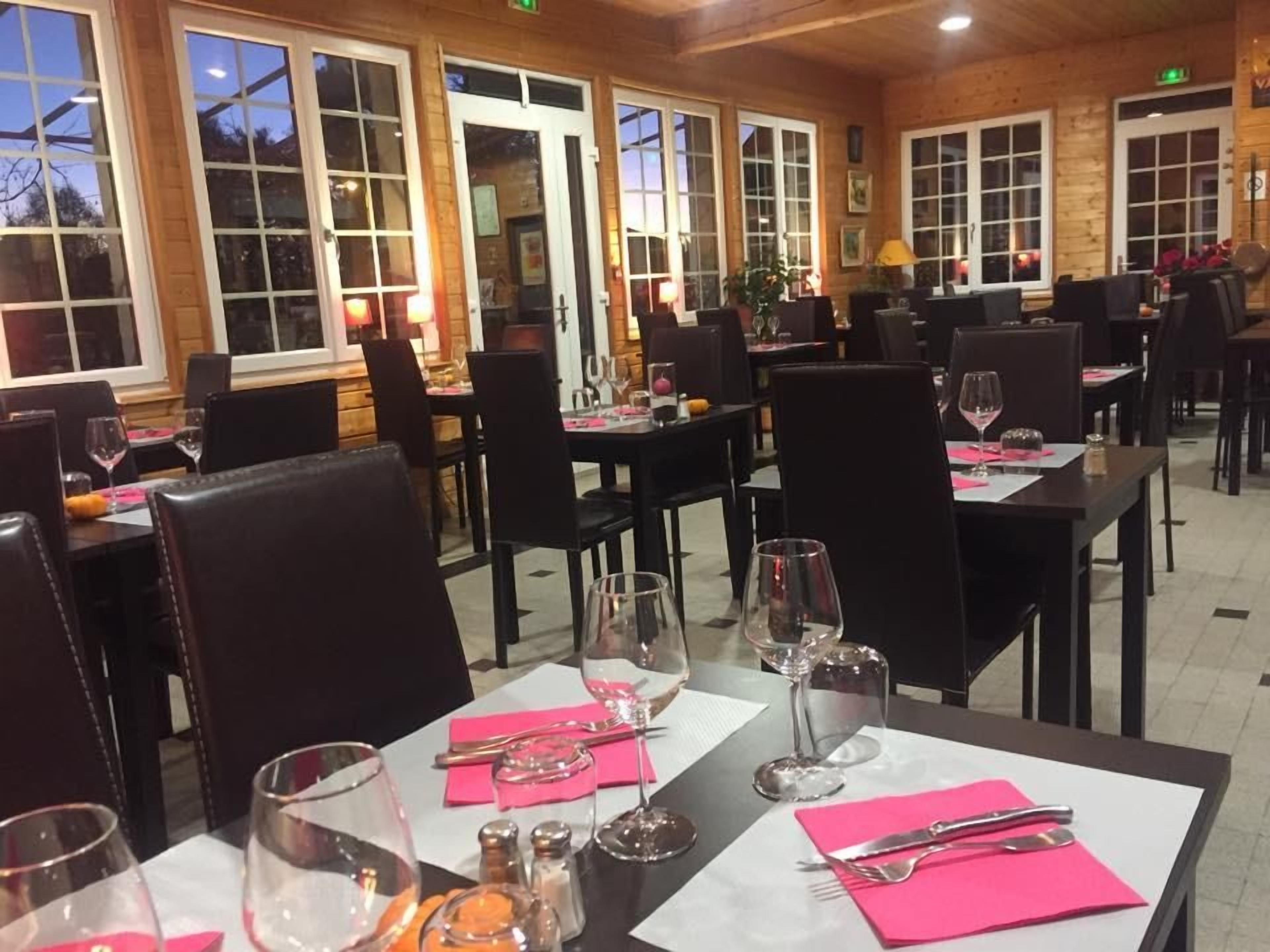 Um restaurante com mesas postas para refeições, cadeiras e vista para o exterior através de grandes janelas.