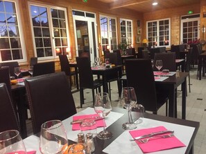 A restaurant with tables set for dining, chairs, and a view of the outside through large windows. - Logis Hotel le 1050 (Saint-Jeure-d'Andaure)