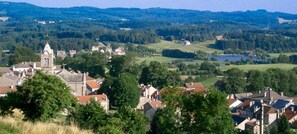 A town with a prominent church, residential buildings, and a lake in the background. - Logis Hotel le 1050 (Saint-Jeure-d'Andaure)