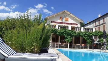 A hotel with a swimming pool, lounge chairs, and a sign indicating it is a restaurant, hotel, and Saint-Acreve.