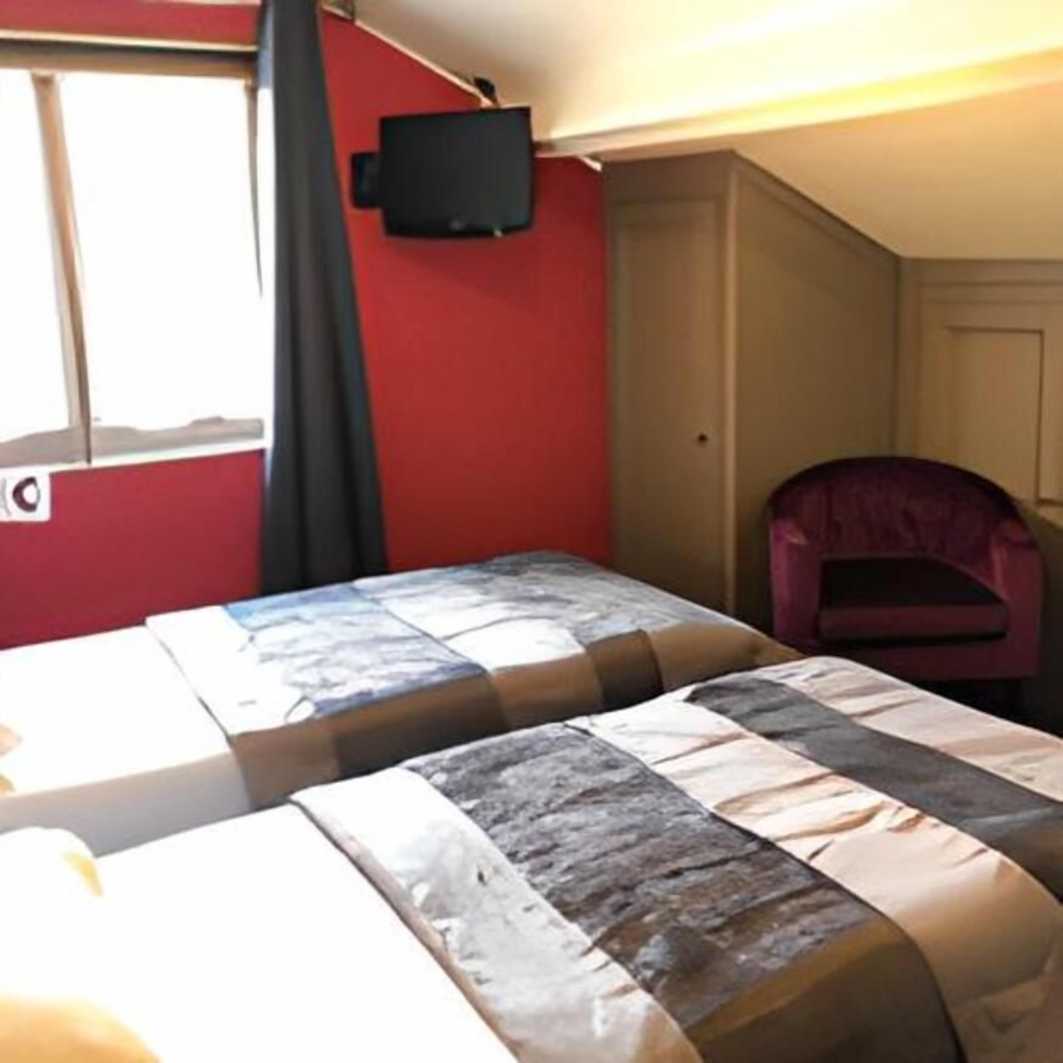 A room with two beds, a television on the wall, and a chair.
