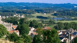 A town with a prominent church, residential buildings, and a lake in the background. - Logis Hotel le 1050 (Saint-Jeure-d'Andaure)