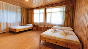 Una habitación con paneles de madera y dos camas, una más grande y otra más pequeña, ambas con ropa de cama y toallas blancas.