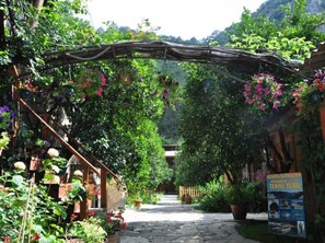 A garden pathway with a wooden pergola, potted plants, and a signboard. - Türkmen Ağaç Evleri (Kumluca)