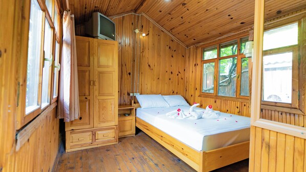 A wooden cabin room with a bed, a TV on a cabinet, and a window with a view of trees. - Türkmen Ağaç Evleri (Kumluca)