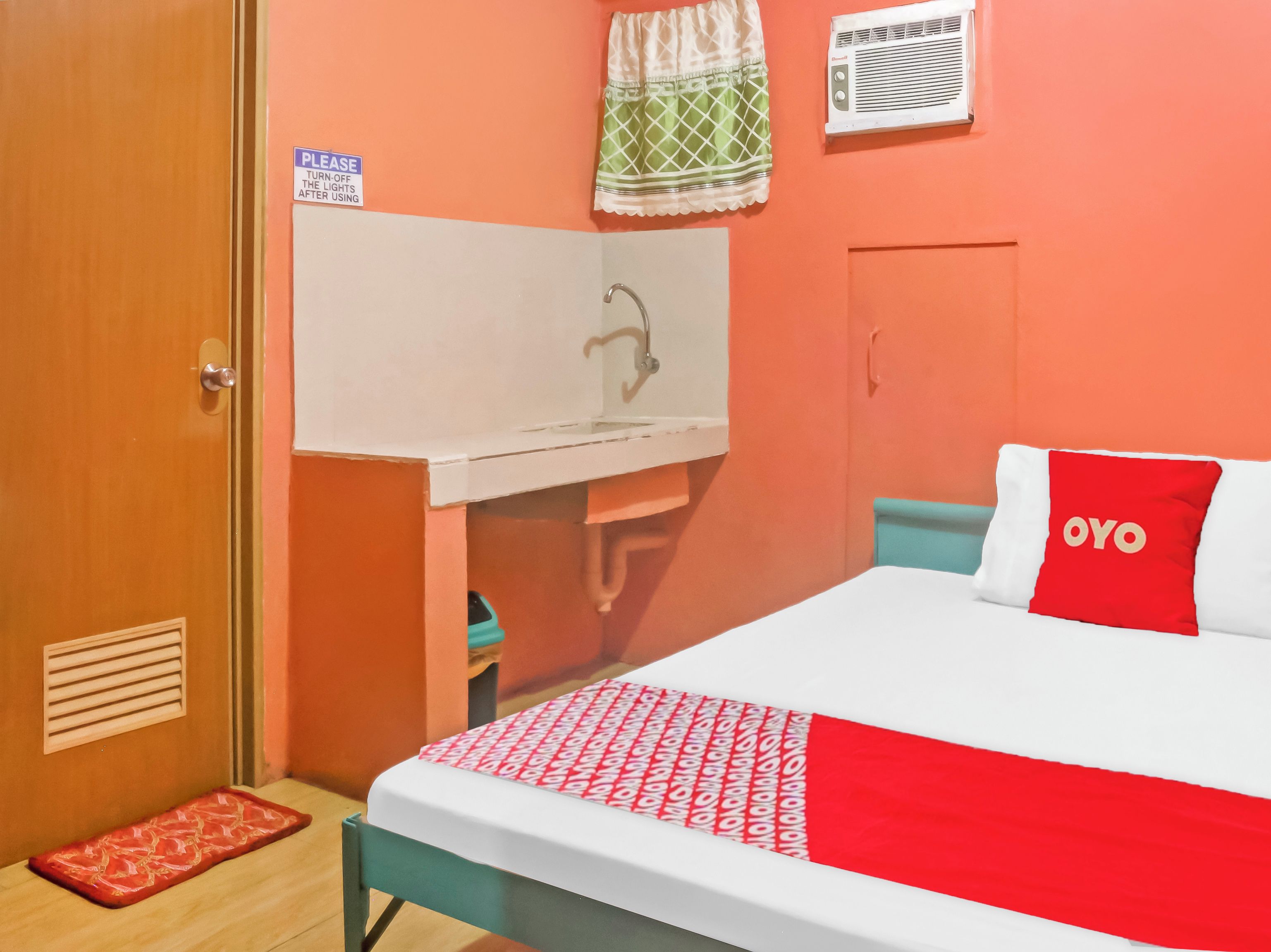 A room with a bed, a small desk, a mirror, and a window with a curtain.